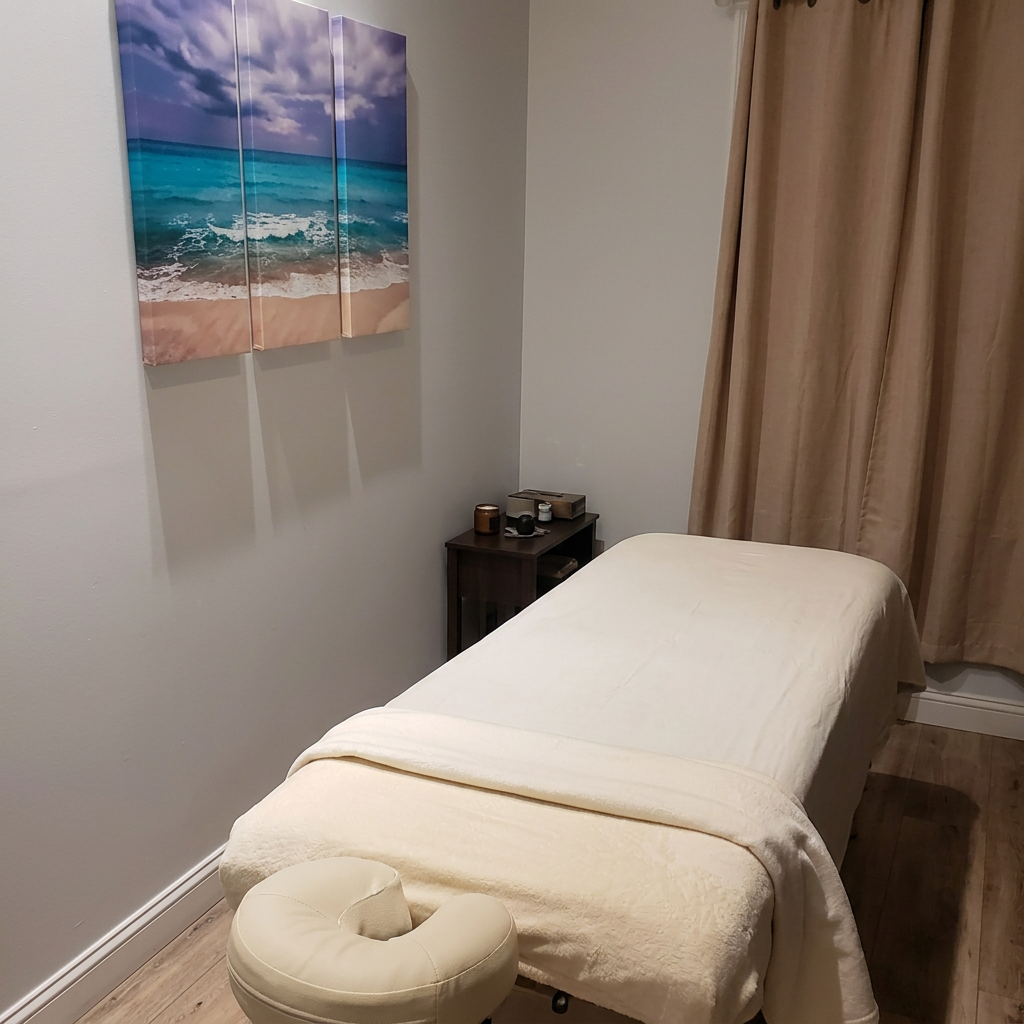 Treatment room with a massage table dressed in cream linens, beach artwork on the wall and soft curtains